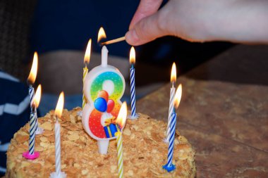 Bir kadının eli pastanın üstünde sekiz numarayla mum yakar. Doğum günü, sekiz yaşında. Holiday, pastadaki mumları üfle..