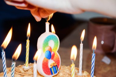 Bir kadının eli pastanın üstünde sekiz numarayla mum yakar. Doğum günü, sekiz yaşında. Holiday, pastadaki mumları üfle..