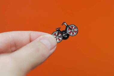 Emaye broş bisiklet elinde turuncu arka planda