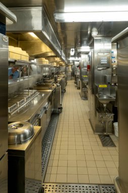 Atlantik Okyanusu - 1 Ekim 2025 Paslanmaz çelik yüzeyleri, profesyonel ekipmanları, lavaboları ve egzoz kaputu olan uzun ve dar bir ticari mutfak temiz ve modern bir ortamda sergilenmektedir..
