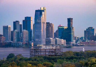 Jersey City, NJ - ABD - 4 Ekim 2025 Jersey şehrinin modern gökdelenleri Hudson Nehri boyunca yumuşak akşam ışıklarını yansıtıyor..