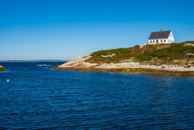 Peggy 'nin Koyu, NS - CA - 29 Şubat 2025 Nova Scotia' da parlak, berrak bir gökyüzünün altında kayalık kıyı şeridi ve mavi sular üzerinde beyaz bir sahil evi duruyor..