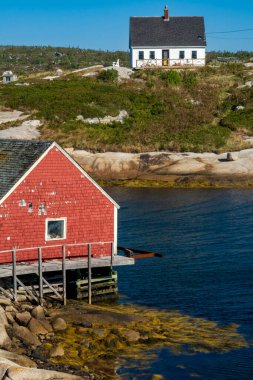 Peggy 'nin Koyu, NS - Sep 29, 2025 Havası çekilmiş kırmızı bir kayıkhane ve kayalık kıyı şeridine bakan beyaz bir tepe evi ve Peggys Koyu, Nova Scotia' nın sakin mavi suları