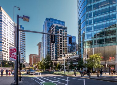 Boston, MA - ABD - 2 Ekim 2025 Boston Liman Bulvarı 'nın güneşli gündüz manzarası, modern cam binalar, ağaçlar ve kaldırımlarda yürüyen insanlar..