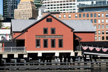 Boston, MA - ABD - 2 Ekim 2025 Boston Çay Partisi Gemileri ve Müzesi, rıhtımda kırmızı bir bina, yakınlarda uzun gemiler ve arka planda modern şehir binaları var..