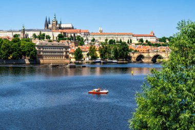 Prag, CZ - 4 Haziran 2023 Prag Kalesi ve Vltava Nehri 'ne bakan Charles Köprüsü manzaralı, sakin sularda sürüklenen küçük bir tekne.