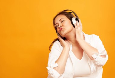 Portakal rengi arka planda, gözleri kapalı, kulaklıkla dans eden genç kızın portresi.