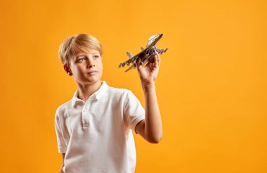 Çocuk turuncu arka planda askeri uçak modeliyle oynuyor.