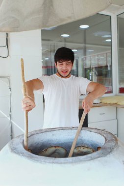 Fırıncı, yeni pişmiş tortillaları büyük kil fırınından çıkarmak için büyük ahşap çubuklar kullanır. Taze ekmek pişiriyorum. Mini fırın konsepti. Uzayı kopyala Dikey fotoğraf.