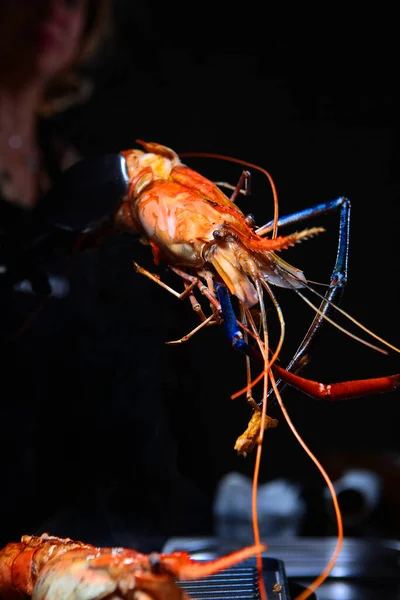 The chef is grilling giant freshwater shrimp. Grilled shrimp in the hands of the cook. Photo on a black background. Unrecognizable person. Cooking concept.