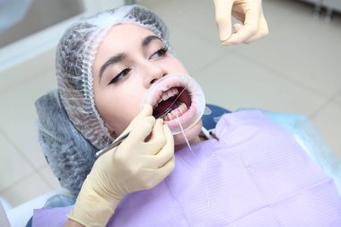 Diş ipiyle interdental alanın profesyonel temizliği. Dişçi randevusunda genç bir kız. Düzgün diş temizliği eğitimi alıyor. Dişeti ve sakız hastalıklarının önlenmesi. Ağızda retraktör var.