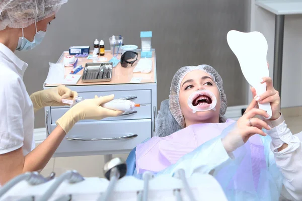 The dentist performs professional dental cleaning and oral hygiene. A young girl at a dentist appointment looks in the mirror.Prevention of caries and gum diseases. Retractor in the mouth.