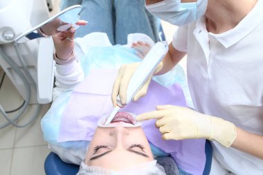Bir dişçi genç bir kız için profesyonel diş temizliği yapar. Elektrikli diş fırçası doktorun elinde. Hasta aynaya bakıyor. Taşıyıcıların önlenmesi. Sağlık kavramı. Üst görünüm.