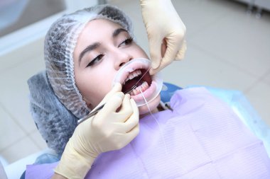 Bir dişçi genç bir kız için profesyonel diş temizliği yapar. Doktorun ellerinde diş ipi var. Hasta aynaya bakar ve dişlerini doğru fırçalamayı öğrenir. Taşıyıcıların önlenmesi. Üst görünüm.