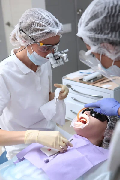 歯科医とアシスタントは 患者のための専門的な歯科清掃を行います 顔の保護スクリーンと医療用マスク 両眼眼鏡 健康の概念 垂直写真 — ストック写真