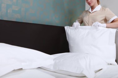 Üniformalı hizmetçi pahalı bir otelin odasındaki yastıkların yastık kılıflarını değiştiriyor. Yastıklar bulanık. Tanımlanamayan kişi. Beyaz pamuk eldivenli eller. Oteldeki kaliteli hizmet kavramı. Otel işleri..