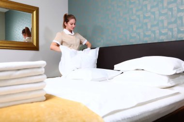 Üniformalı bir hizmetçi çarşafları değiştiriyor. Pahalı bir otelde oda temizliği. Beyaz pamuk eldivenli eller. Otel işi kavramı. Havlular odak dışı. Boşluğu kopyala.