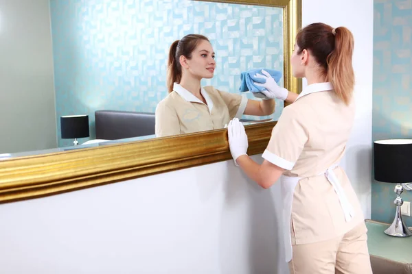 制服を着たメイドが鏡でフレームを拭く 高価なホテルの部屋の掃除 白い綿の手袋で手 鏡の中の反射 ホテルビジネスのコンセプト スペースのコピー — ストック写真