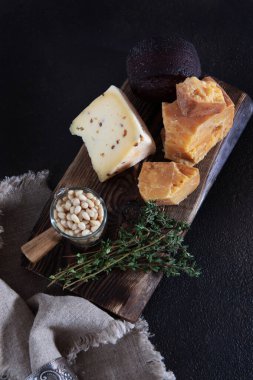 Tahtada bal ve çam fıstığı olan çeşitli peynir çeşitleri. Ev yapımı el yapımı peynir. Süt doğal bir üründür. Siyah arka planda dikey fotoğraf. Üst görünüm.