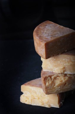 Uzun ömürlü sert peynir parçaları dikey olarak dizilmiştir. Durgun yaşam kavramı. Siyah arka planda dikey fotoğraf. Boşluğu kopyala.