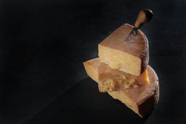 Siyah arka planda uzun ömürlü sert peynir parçaları. Peynir dikey sıra halinde istiflenmiş. Durgun yaşam kavramı. Doğal süt ürünü. Boşluğu kopyala.