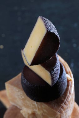 Ekstra şaraplı peynir ve koyu bir arka planda klasik sert peynir. Peynir dikey sıra halinde istiflenmiş. Hayat konsepti. Doğal süt ürünü. Dikey fotoğraf.