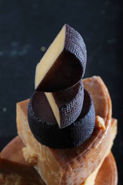 Uzun yıllanmış peynir parçaları. Peynirin katı dokusu. Koyu arkaplanda güzel kokulu peynirler. Dikey fotoğraf. Kırmızı şarap eklenmiş peynir..