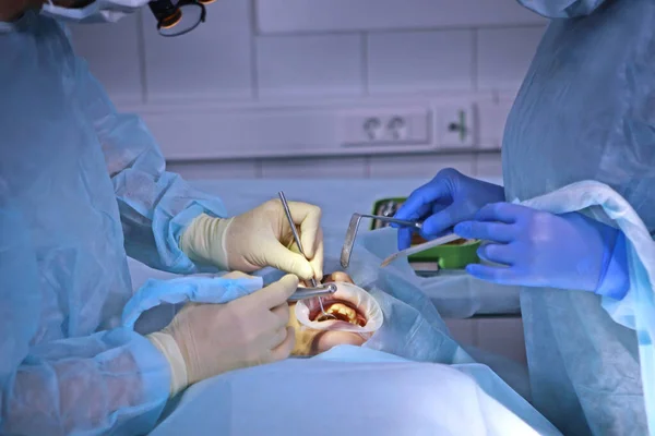 Operation in einer Zahnklinik. Der Chirurg und der Assistent. Moderne Zahnmedizin. Foto im Operationssaal. Das Konzept der Gesundheitsversorgung. Hände in Schutzhandschuhen. Menschen sind nicht wiederzuerkennen. — Stockfoto