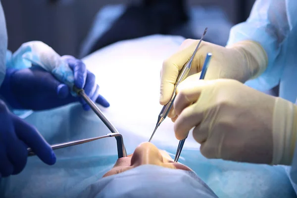 Bir diş kliniğinde ameliyat. Cerrah ve asistan. Modern dişçilik. Ameliyathanede fotoğraf var. Sağlık hizmetleri kavramı. Ellerinizi koruyucu eldivenlere koyun. İnsanlar tanınmaz halde..