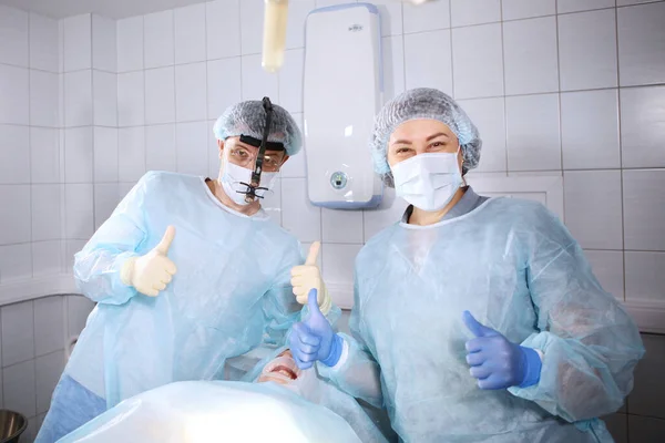 Dental surgeon and an assistant in the operating room. Doctors smile after a successful operation . Funny doctors. Unrecognizable patient.