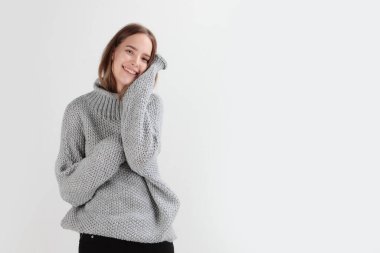 Gri yün kazaklı genç bir kız. Işık arkaplanındaki fotoğraf. Sıcak giysi kavramı. Uzayı kopyala Doğal yünler. Soğuk mevsim kıyafetleri..