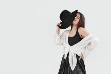 Genç, neşeli bir esmer elinde siyah bir şapka tutuyor. Kızın kıyafetleri siyah ve beyaz. Boşluğu kopyala..