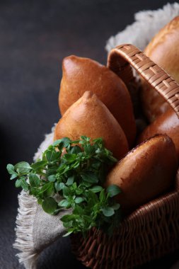 Hasır sepette turta şeklinde hamur işleri. Yeşil fesleğen. Karanlık bir arka planda fotoğraf. Dikey fotoğraf. Üst görünüm.