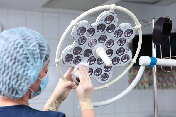 Klinikte tıbbi malzemelerin dezenfekte edilmesi. Koruyucu eldivenler ve tıbbi maske takan bir diş hekimliği çalışanı ameliyat odasındaki ekipmanları siler. Ameliyathanede LED lamba.