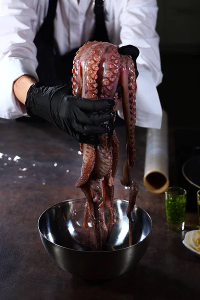 Cooking octopus. A whole octopus in the hands of the chef.An unrecognizable person. Seafood dishes. Protein food.Vertical photo inside room.