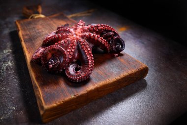 Ahtapotu ahşap bir kesme tahtasının üzerinde haşladım. Deniz ürünleri pişirmek. Karanlık arka plan. Protein yiyeceği. Boş alan. İnsansız fotoğraf.