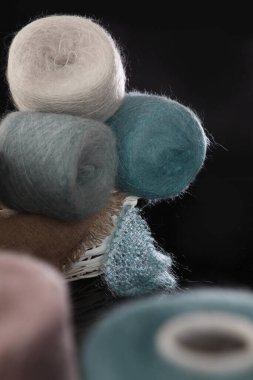 El örgüsü için yumuşak yün ipliği beyaz hasır sepetin içinde bulunur. Farklı renklerde iplik, doğal saç motifi. Hobiler ve el işleri. Siyah arka plan. İplik derileri odak dışı.