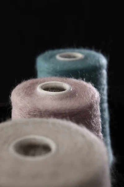 Large bobbins with wound yarn for hand knitting. Soft fluffy coat. Hobby and manual labor. Vertical photo on a black background. Out of focus.