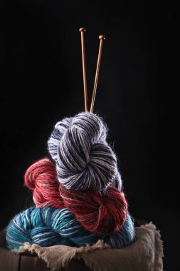Siyah arka planda örgü iğneleri olan renkli yün iplik. El örgüsü için iplik. Hobi kavramı. Boş alan. Dikey fotoğraf.