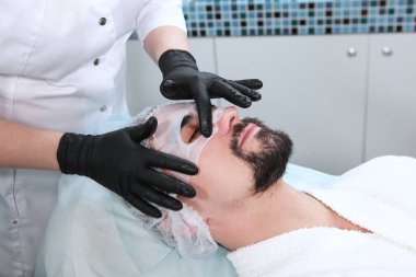 Adamın biri kozmetoloji kliniğinde maske yapıyor. Erkek kozmetolojisi. Modern bir adam. Gençliği koruma ve yüz derisi ile ilgilenme kavramı..