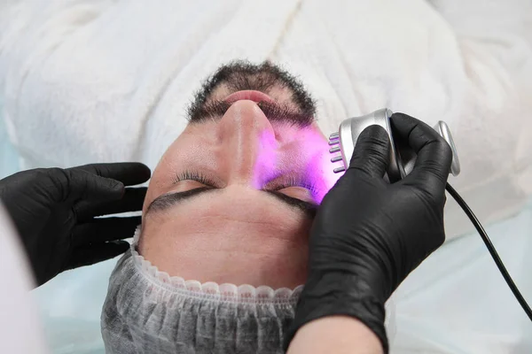 Adamın biri kozmetik kliniğinde yüz maskesi yapıyor. Erkek kozmetolojisi. Kozmetik kliniğinde bir adam. Gençlik koruma ve cilt bakımı kavramı. Yakın çekim. Üst görünüm.