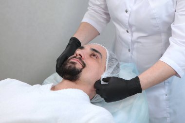Kozmetoloji kliniğinde bir adam prosedüre hazırlanıyor. Erkek kozmetolojisi. Yüz temizleme. Gençlik koruma ve cilt bakımı kavramı. Yakın plan.
