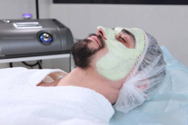Bir adamın yüzünde kozmetik maske. Kozmetik kliniğinde yüz ameliyatı yapan bir adam. Erkek kozmetolojisi. Gençliğin korunması ve cilt bakımı kavramı.