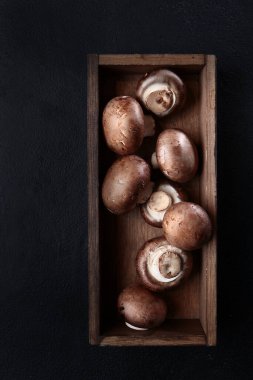 Tahta bir kutuda kraliyet şampiyonu mantarı. Tahta bir kutuda birkaç taze mantar. Üst Manzara. Uzayı kopyala Siyah arkaplandaki fotoğraf. Dikey fotoğraf