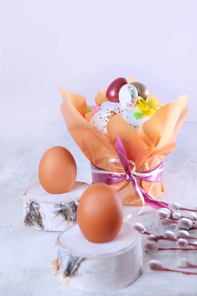 Easter cake in a festive package on a light background. Willow branches.Easter holiday. Free space. Chicken eggs on wooden stands. Vertical photo.