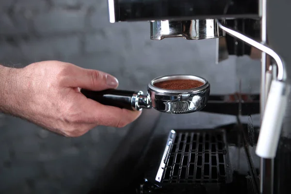 Coffee filter holder or coffee horn in the barista\'s hand. The coffee machine is out of focus. Ground fresh coffee.