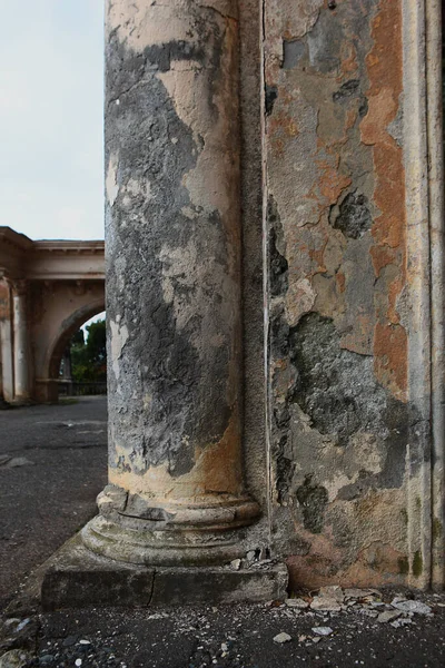 Vernietigde architectonische structuur. Kolommen van beton. Diepe scheuren en afbrokkelende pleister. Een ruime vertakte scheur in een oude betonnen kolom.Verticale foto. — Stockfoto