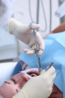 Dişçi anestezi iğnesi yapar. Elleri lastik eldivenli ve şırıngalı. Ağzını aç. Ağızda retraktör. Ağrı kesici. Diş implantı yerleştirmeye hazırlanıyor..