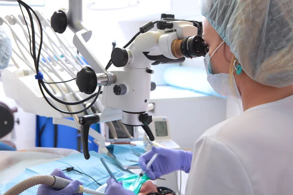 Microscópio dentário. Tratamento da inflamação da raiz do dente. Odontologia moderna. Vista lateral. O médico lava os canais radiculares. Uma pessoa irreconhecível. — Fotografia de Stock