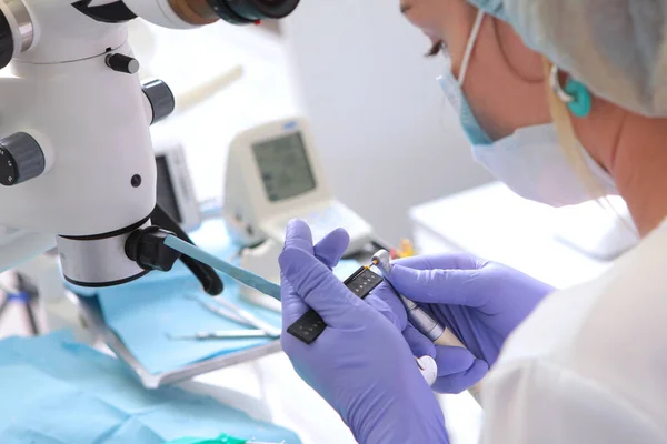 Uma broca para penetrar nos canais dentários. O médico mede o comprimento da broca. Close-up. Mãos em luvas de proteção.Tratamento dentário.Fora de foco — Fotografia de Stock